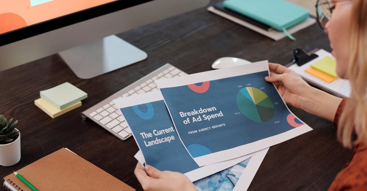 A businesswoman reviews marketing documents with charts at her desk, featuring a computer and office supplies.
