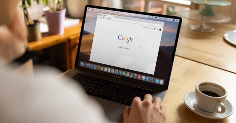 An adult using a laptop indoors, browsing Google at a wooden table with coffee.